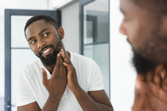 At home in bathroom, African American man checking his beard in mirror