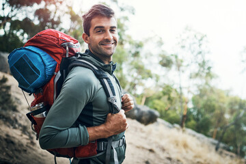Hiking, portrait or fitness man with backpack in forest for wellness, peace and morning cardio in nature. Sport, smile and happy athlete explorer in park for exercise, training or travel adventure