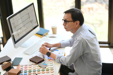 Experienced senior interior designer in eyeglasses working on new project at creative office