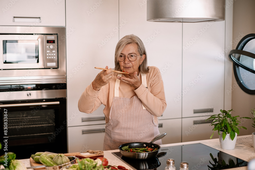 Wall mural smiling woman at home tasting food from the pan with a table spoon. people in the kitchen preparing 