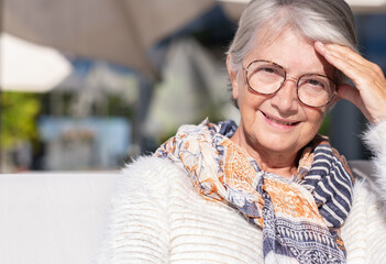 Portrait of beautiful senior woman gray haired sitting outdoors in a sunny day looking at camera smiling. Serene retirement lifestyle concept