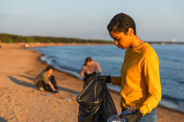 Earth day. Volunteers activists team collects garbage cleaning of beach coastal zone. Woman puts...