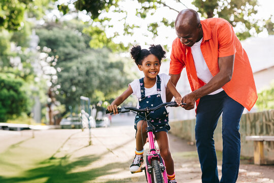 Happy father teaching daughter to ride bicycle in park