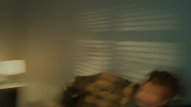 Handheld slowmo of young Caucasian man going through anger attack, throwing stuff and punching wall. He falling in bed exhausted at night