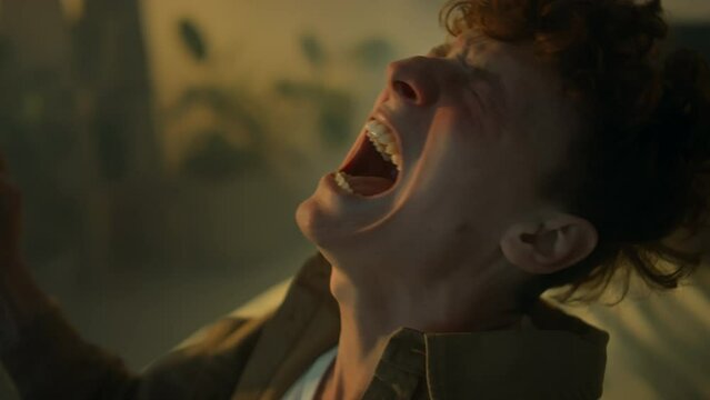 Side closeup of nervous Caucasian guy shouting at night while alone at home. Feeling hopelessness, despair and anguish