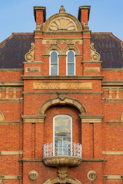 A tall brick facade of an historic town hall building with a fenced balcony and decorative rendering