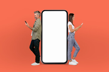 Energetically, the middle aged couple engages with viewers, standing next to a mockup smartphone...