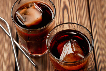 Two glasses of cola with ice on a wooden background.