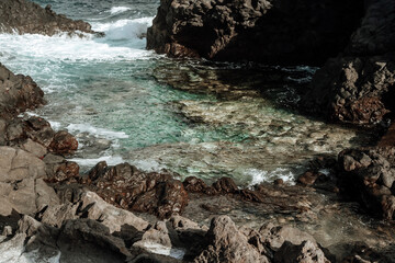 A rocky shoreline with a small body of water. The water is clear and calm, and the rocks are jagged and rough. The scene is peaceful and serene, with the water reflecting the sky