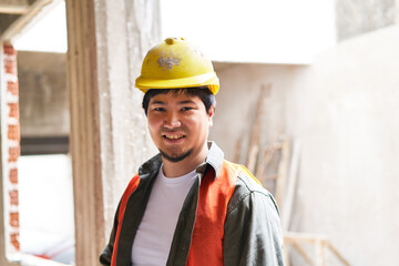 Portrait of smiling young male bricklayer wearing hardhat and safety vest at construction site