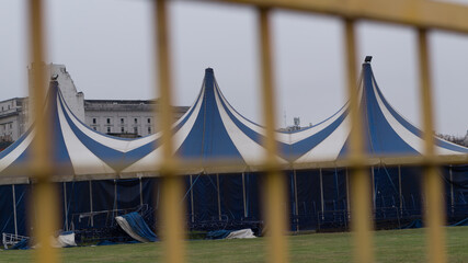 A blue and white circus tent against a gray sky.