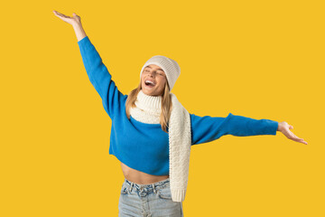 A cheerful woman is dressed in a blue sweater, white scarf, and beanie, celebrating with both arms...