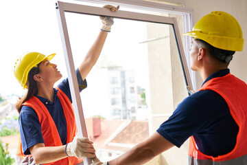 Two carpenters wearing safety workwear installing window frame together in house construction site