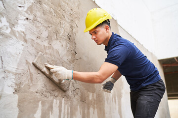 Young male labor plastering on wall with cement at construction site