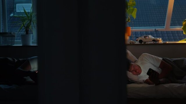 Sad and depressing view on modern couple after an argument, each one in different room spending time on their phone in darkness instead of communicating. Screen time in relationship