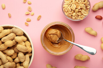 Jar and spoon of peanut butter on pink background.