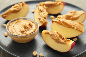 Slices of fresh apple with peanut butter in bowl on dark plate.