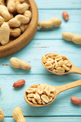 Peanuts in spoon on blue wooden background. Vertical photo