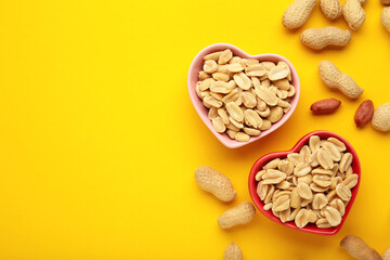 Peanuts in a heart shaped bowl on yellow background.