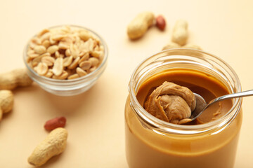 Jar and spoon of peanut butter on beige background.