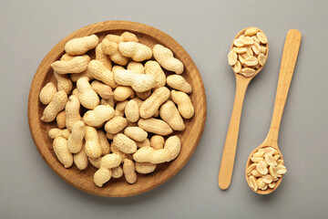Fresh healthy peanuts in bowl and spoon on grey background.