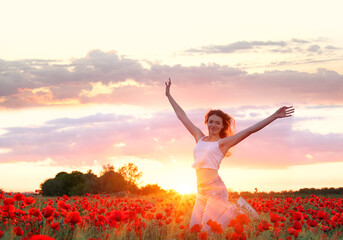 Beautiful young girl jumping in flower poppy field at sunset. Beautiful landscape with lots of red...