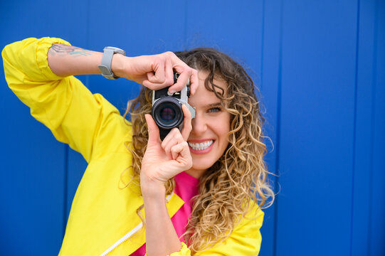 Happy woman photographing through camera in front of blue wall