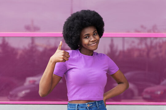 Smiling woman showing thumbs up standing in front of magenta window
