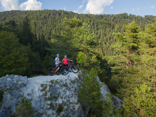 Biker couple after electric mountain bike ride enjoying the spectacular view and success, aerial view.