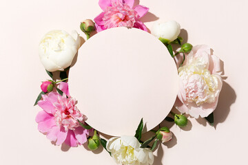 Round shaped frame for text or object and pink and white peonies on a beige background. Top view.