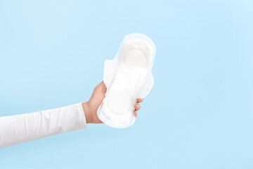 The girl holds a sanitary pad in her hand on a blue background. Period. Top view.