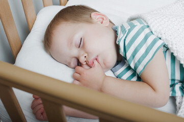 Toddler boy sleeping with a finger in his mouth close-up on bed. Health care concept