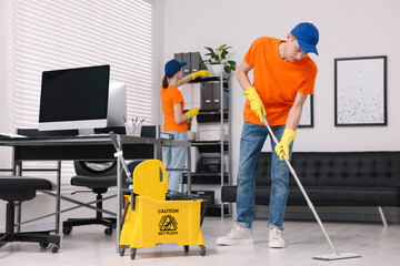 Cleaning service workers cleaning in office. Bucket with wet floor sign indoors
