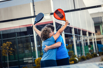 Mixed adult couple celebrate winning the point in padel on outdoor court.