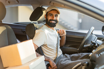 A bearded Indian man is sitting in the drivers seat of a car, smiling while fastening his seatbelt....