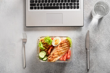 Lunchbox with healthy salad and glass of water in office on gray table. Healthy eating on work. View from above.