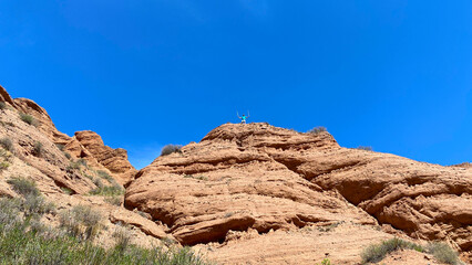 Fototapeta premium A man stands on top of a rocky hill, admiring the scenery. The red canyons of Konorchek. Travel to Kyrgyzstan. The sky is clear and blue