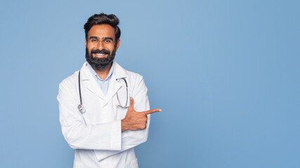 A cheerful Indian doctor with a dark beard and a stethoscope around his neck is pointing to his...