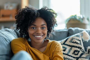 Fototapeta premium A relaxed and cheerful young woman with a bright smile sits comfortably at home on a sofa