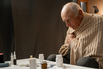 sick man, wrapped in blanket, is looking at what pills to take for his illness. Treatment for viruses.