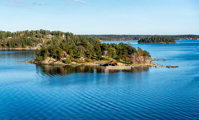 Naklejka premium Small island connected with a bridge in Stockholm archipelago in Baltic sea with traditional white and red house at sunny spring evening scenery.