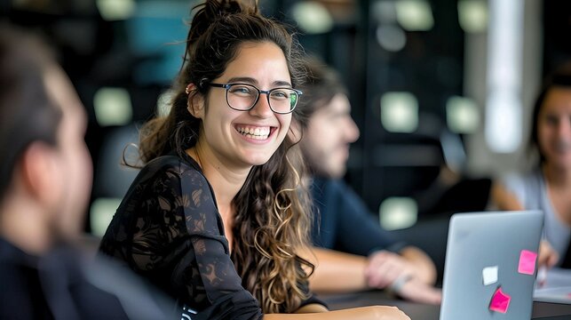 Smiling woman wearing glasses, working in a modern office environment, highlighting a collaborative and joyful workspace.