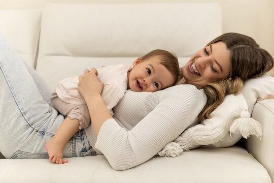 A toddler girl is lying on her mother with a playful expression while her mother smiles happily