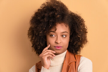 thoughtful african american woman thinking and looking to the side in beige studio background....
