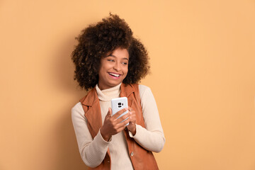 joyful afro brazilian woman watching video and photos on mobile smartphone in all beige colors....