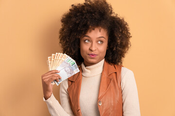 happy black young woman showing money, brazilian Real in beige studio background. financial,...