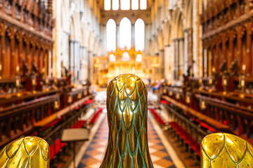 Shallow focus of the magnificent gold eagle seen on the lectern of a famous English cathedral. The large alter and choir seating can clearly be seen.
