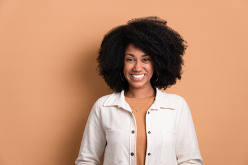 pretty african american woman smiling and looking at camera wearing white jacket in beige studio...