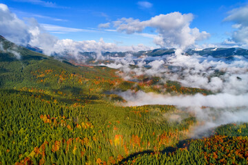 Fototapeta premium Fog spreads over the mountains at dawn. The sun rises on the horizon. Carpathians in the morning. Aerial drone view.