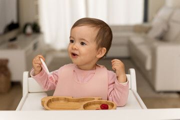 Adorable toddler girl wears a pink bib while eating fruit